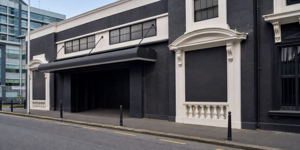 Dark city street facade with a large black awning over an open doorway and white decorative trim along the walls