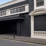 Dark city street facade with a large black awning over an open doorway and white decorative trim along the walls