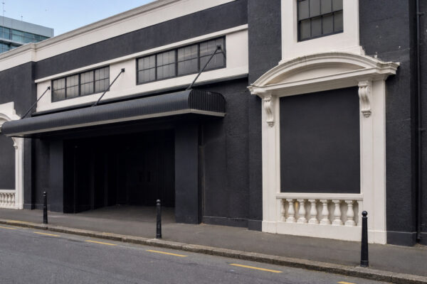 Dark city street facade with a large black awning over an open doorway and white decorative trim along the walls