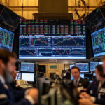 Stock trading floor with a wall of monitors showing stock charts and market data traders at desks in the foreground